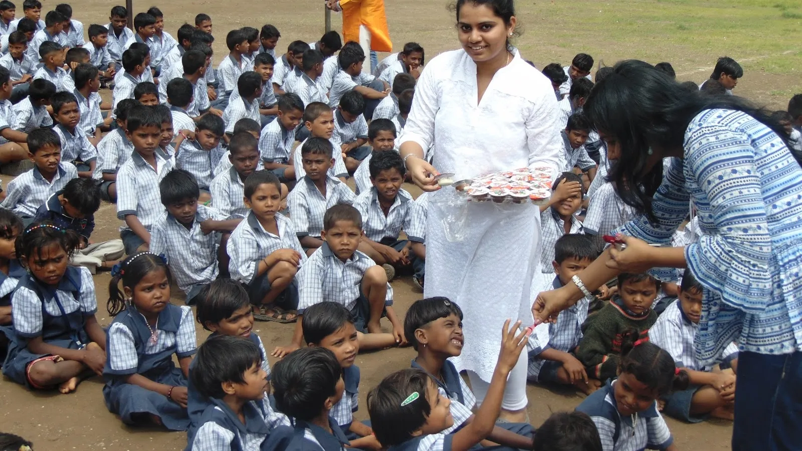 Volunteers handing out treats to uniformed schoolchildren seated on a school ground in India