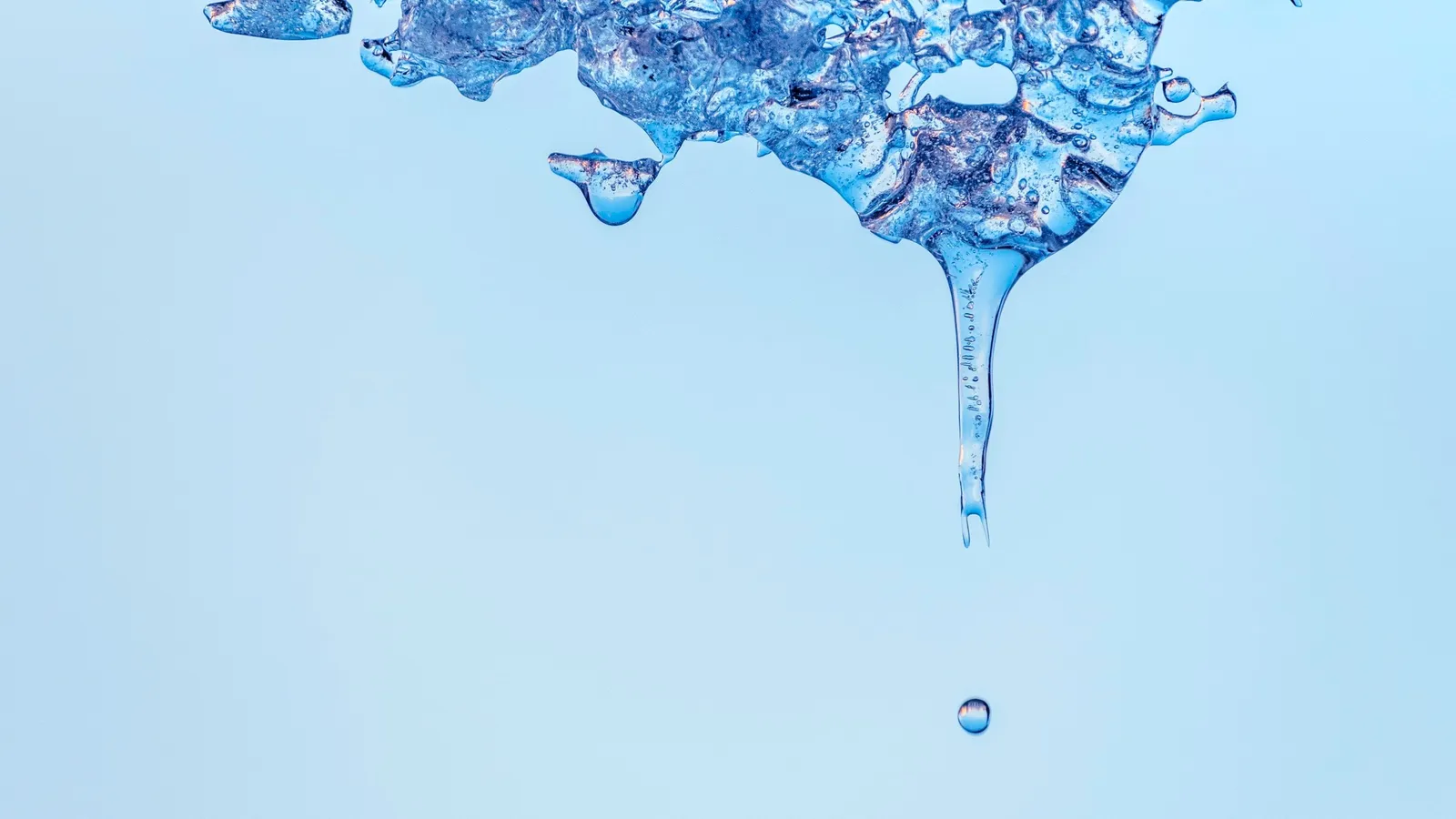 Water dripping from melting ice against a pale blue background