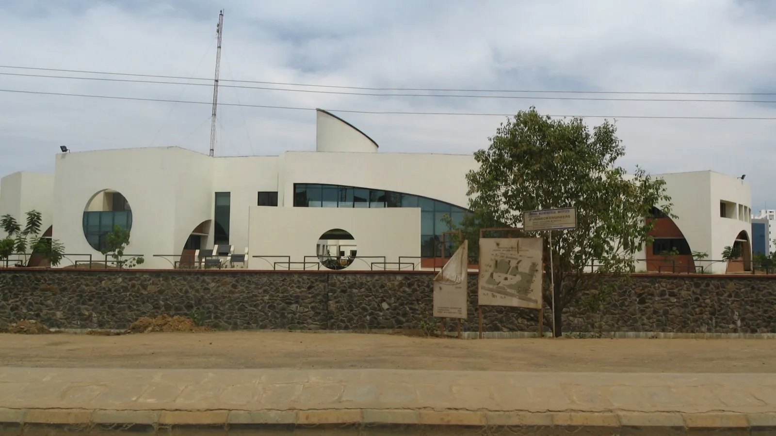 White main building of the Chennai Mathematical Institute with round windows, behind a stone wall