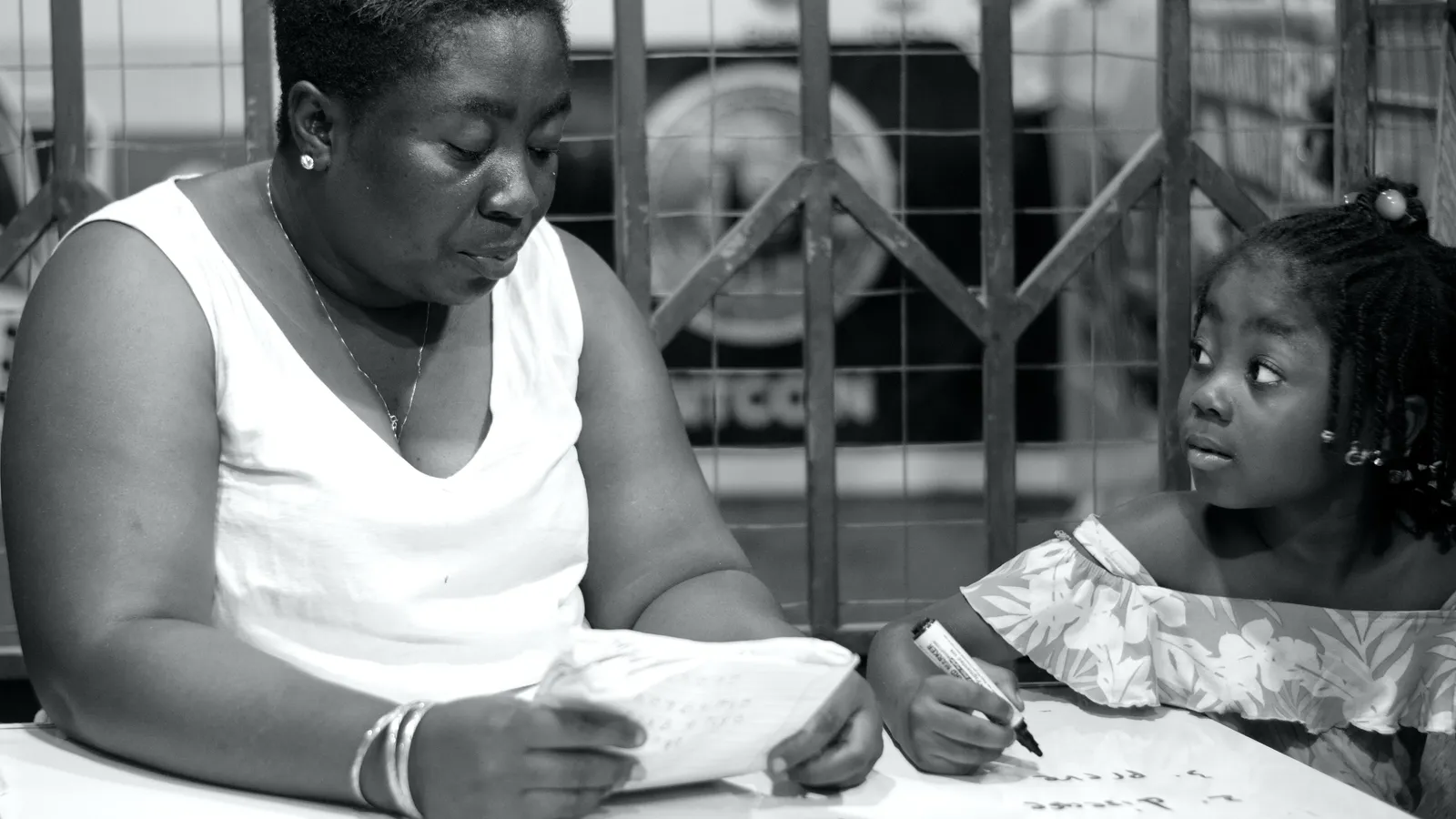 Young girl holding a marker looks up at a woman reading her homework sheet