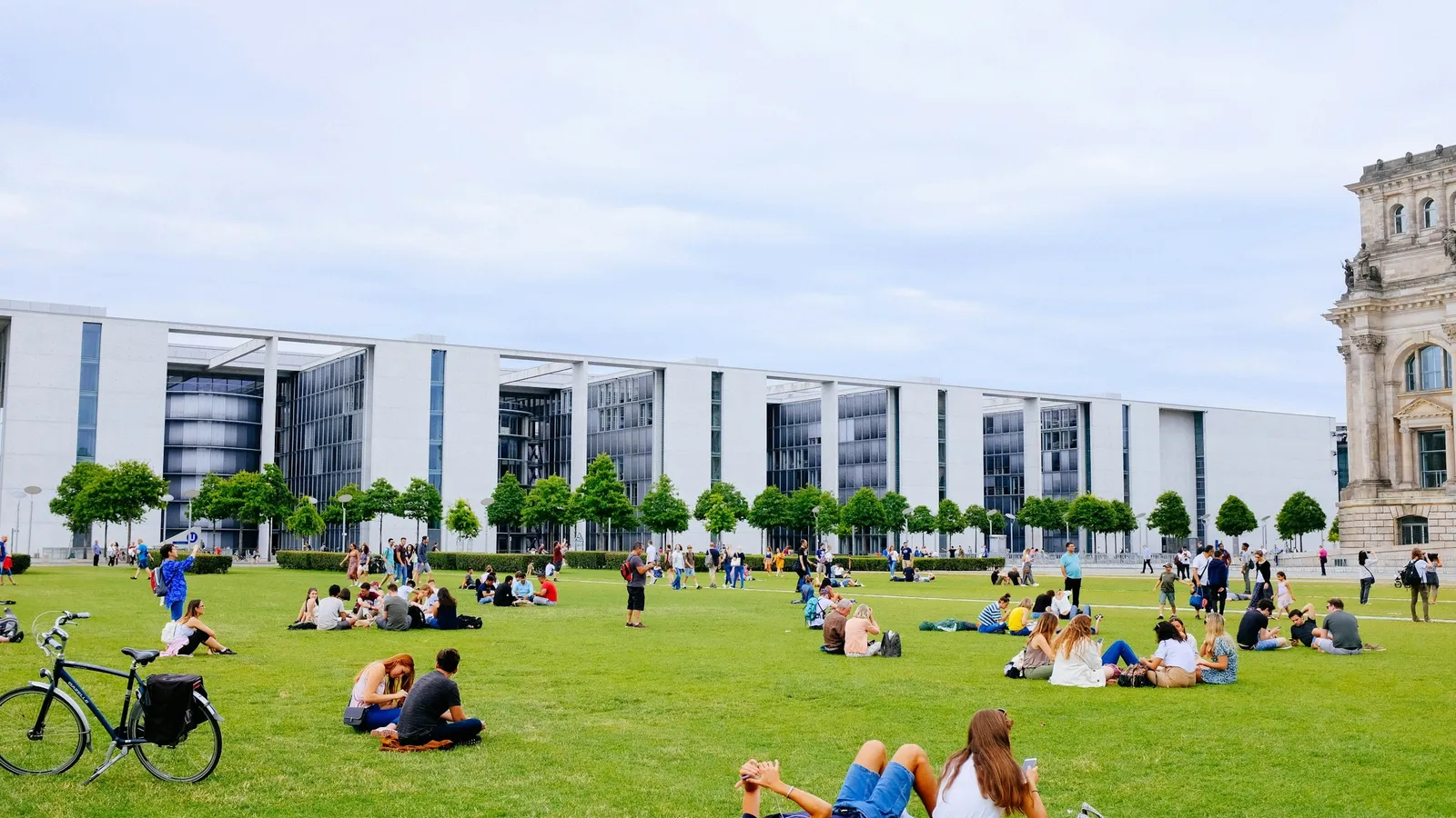 Young people relaxing on a sunny lawn beside modern glass buildings