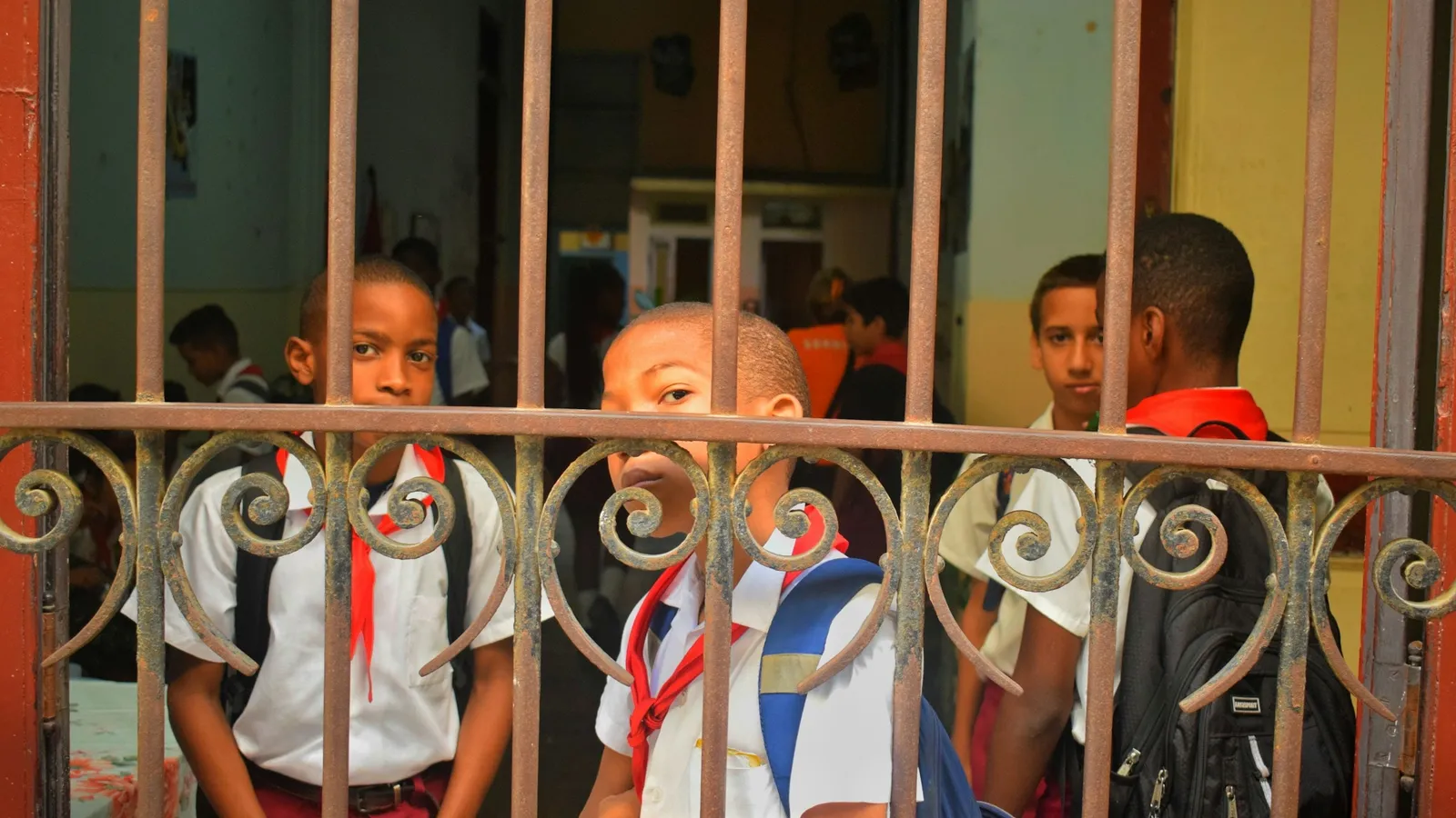 Young schoolboys in uniform standing behind a metal school gate