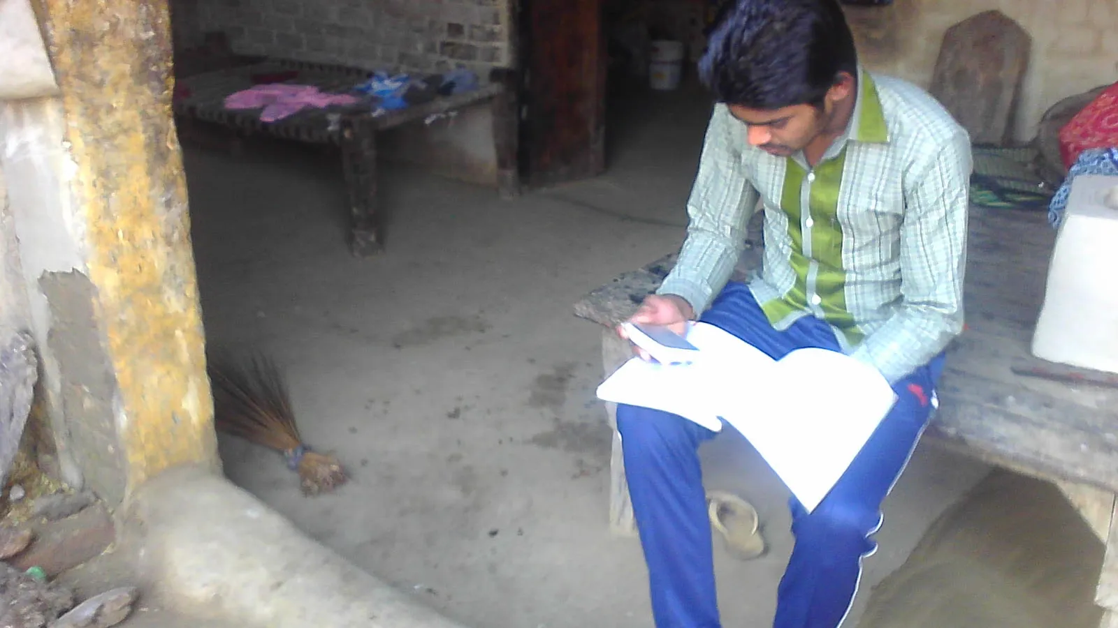 Young student on a wooden bench looking at a phone, papers open on his lap