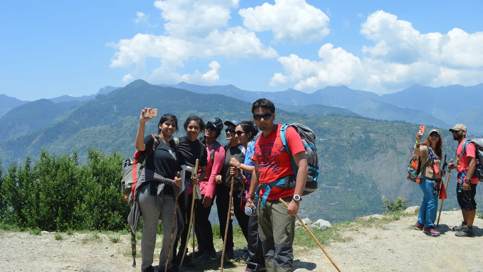 Young trekkers with backpacks and walking sticks take a selfie on a mountain trail in India