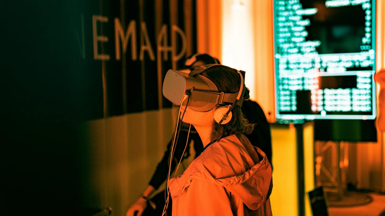 Young woman in a VR headset beside a screen showing code